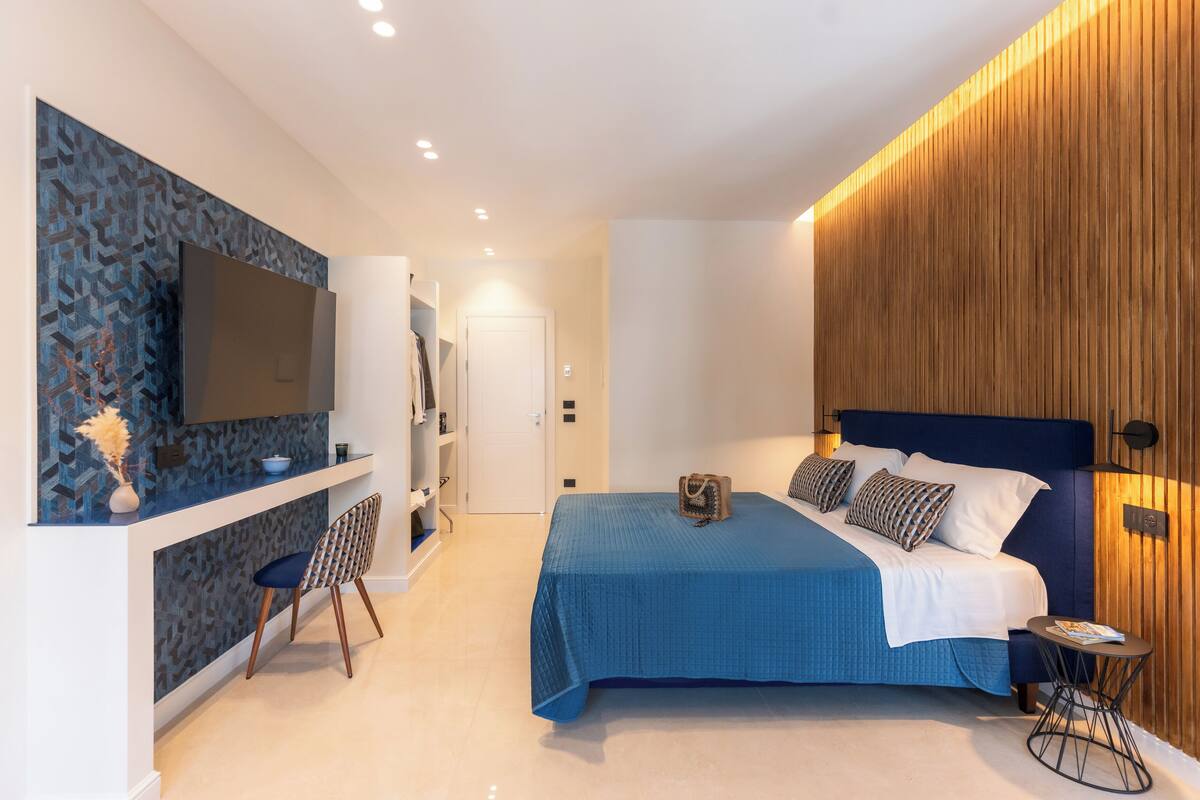 Une chambre à coucher moderne avec un grand lit, un téléviseur fixé au mur et un mur d’accent en bois.