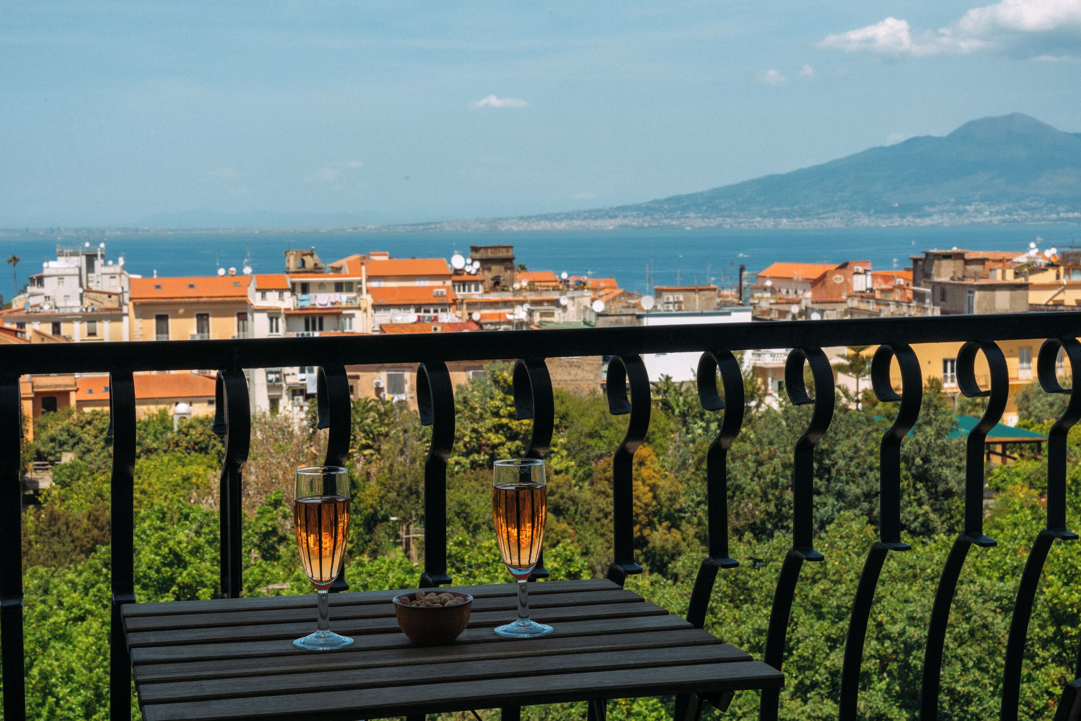 Un balcon avec une table, deux verres contenant une boisson et un bol de noix.