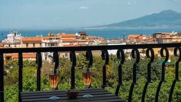 Un balcon avec une table, deux verres contenant une boisson et un bol de noix.