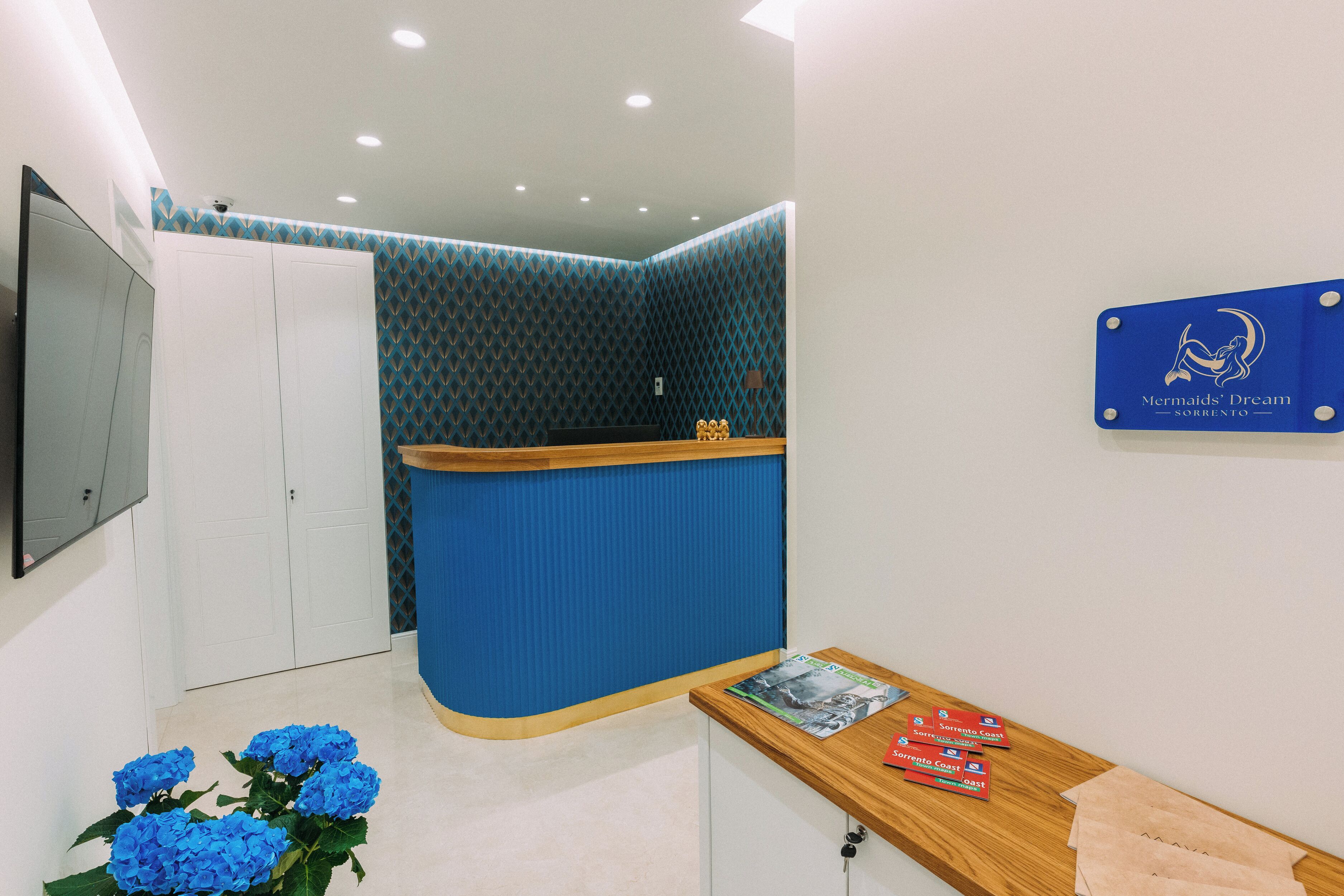 A reception area with a blue counter, a wooden desk, and a blue wall with a geometric pattern.