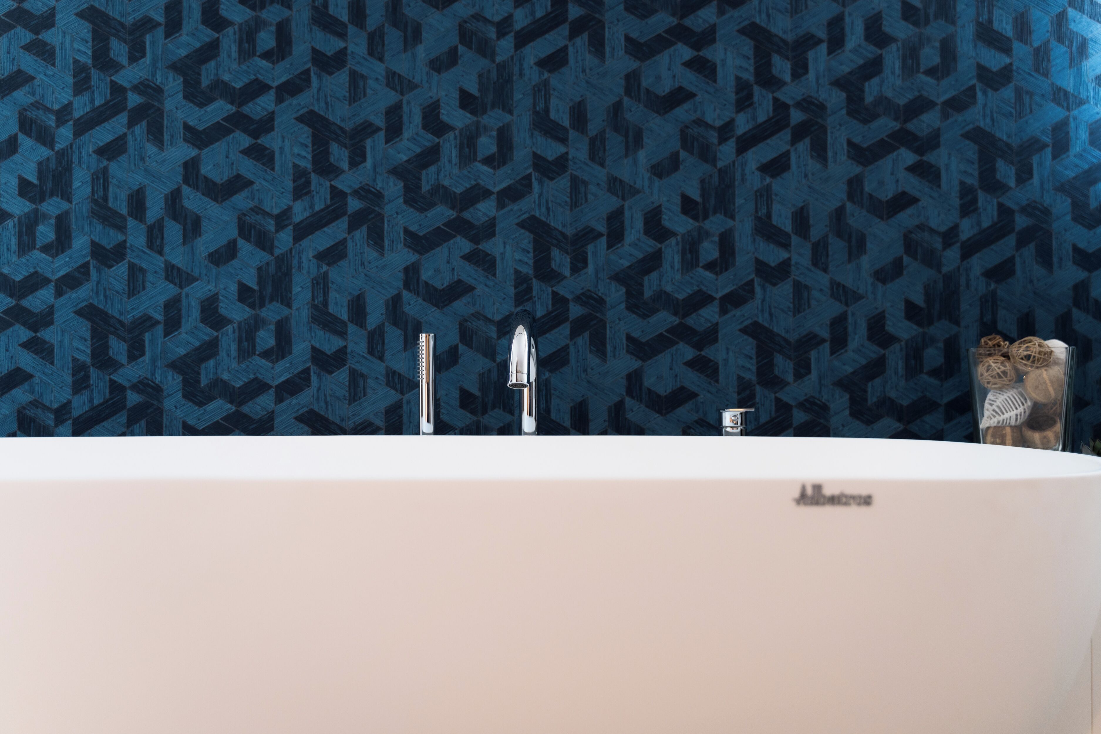 A modern bathroom with a geometric patterned wall, a white bathtub, and two faucets.