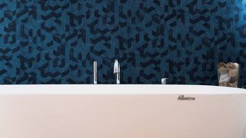 A modern bathroom with a geometric patterned wall, a white bathtub, and two faucets.