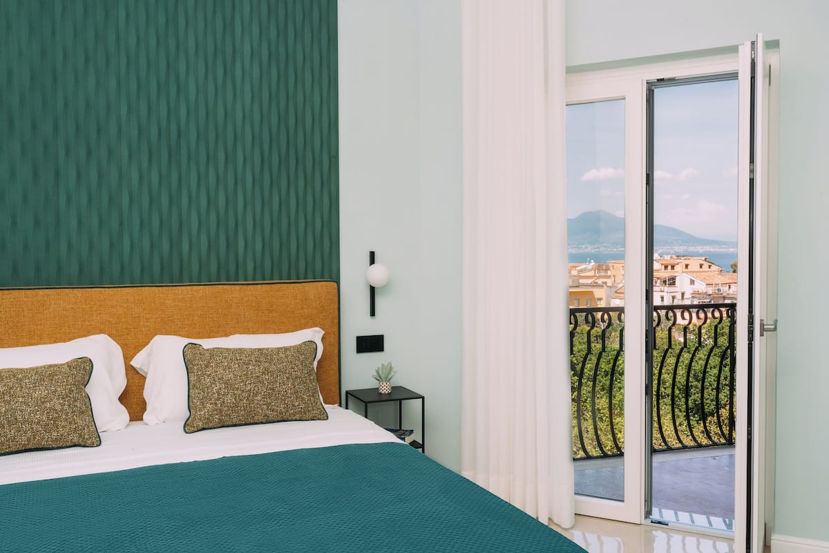 Une chambre avec un grand lit, une table de chevet et une vue sur un balcon doté d’une balustrade.