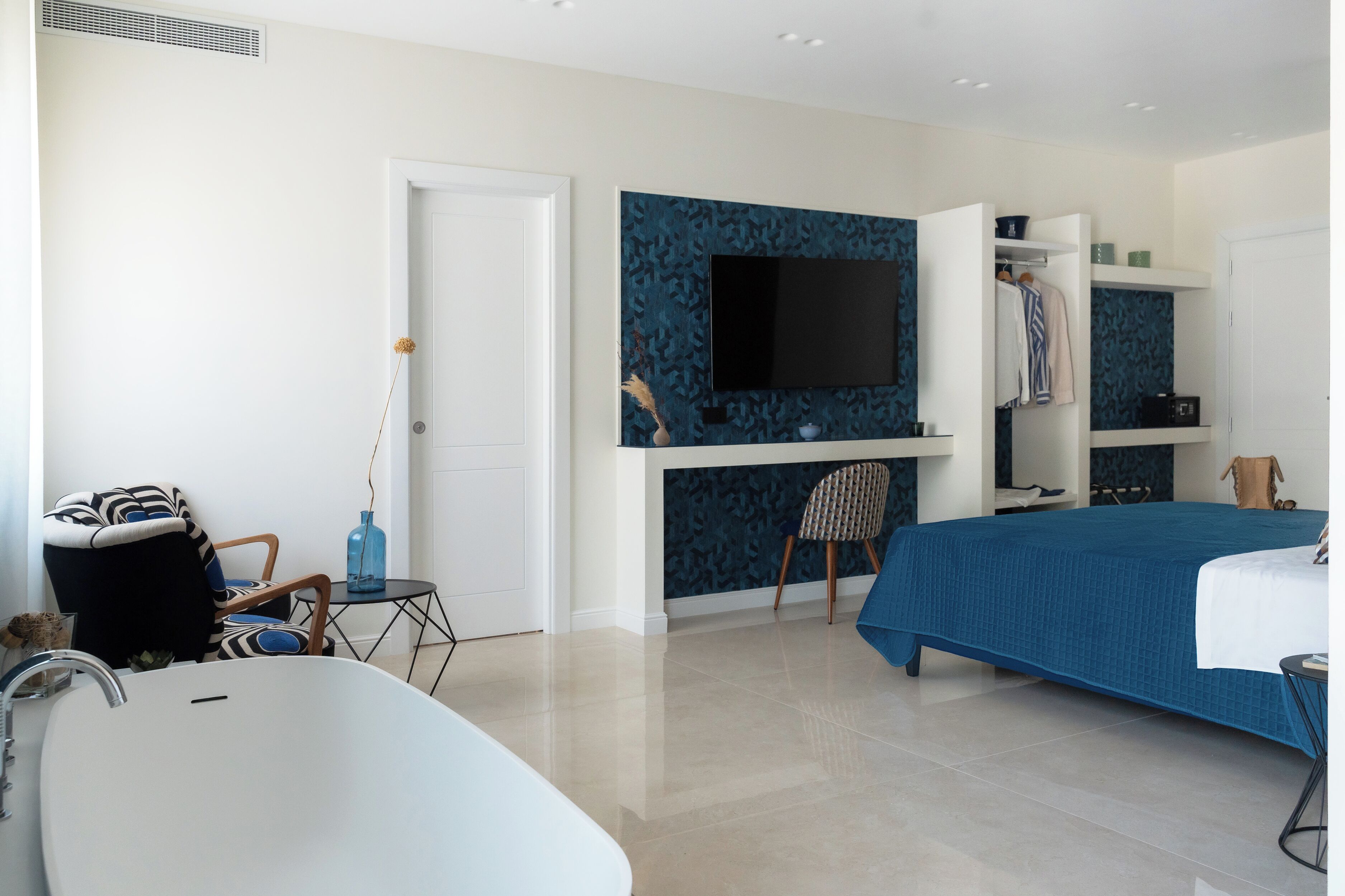 Une chambre à coucher moderne avec un grand lit, un téléviseur fixé au mur, une chaise et une petite table.