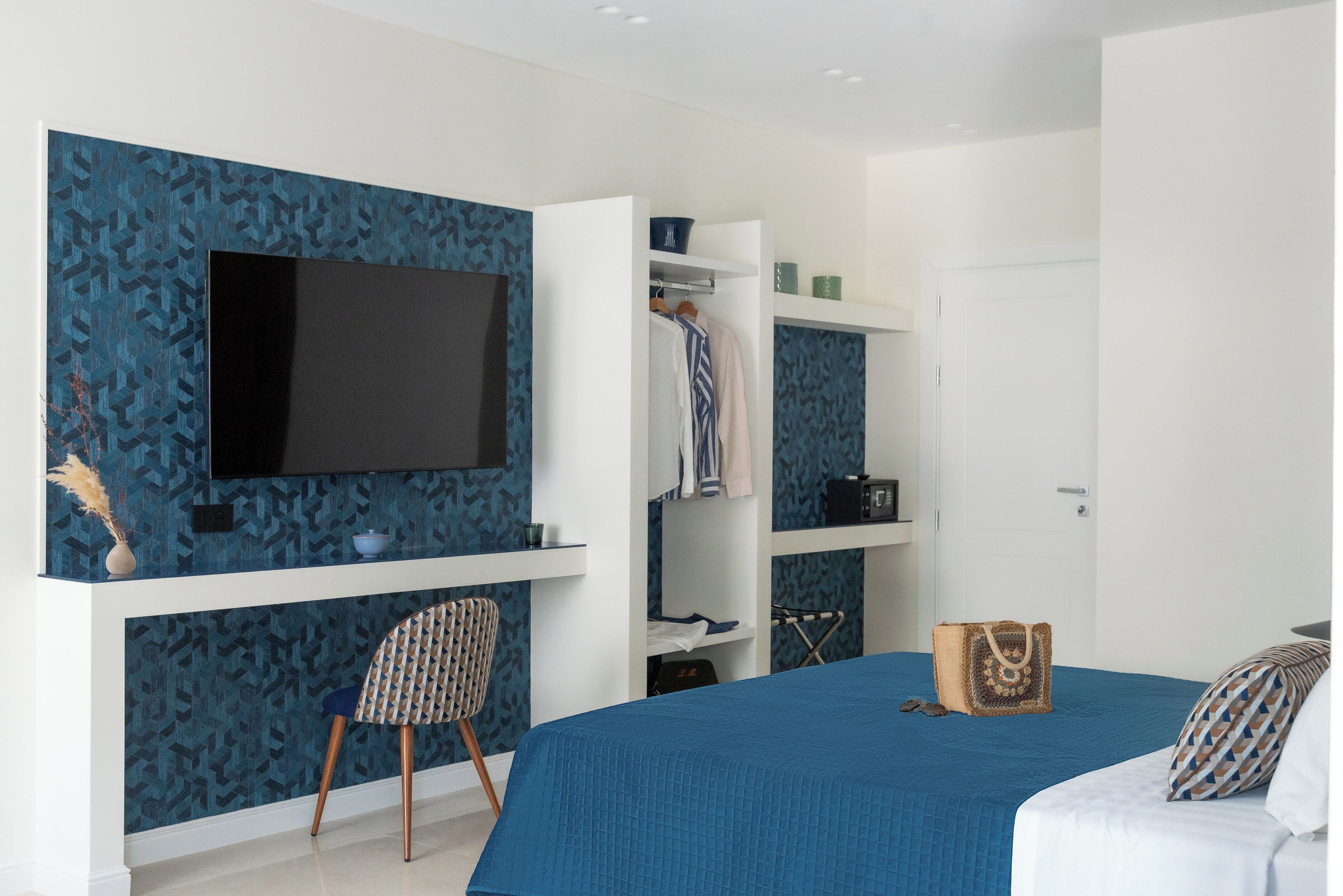 Un dormitorio con cama, televisión montada en la pared, armario y una silla.