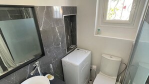 Un baño moderno con un lavabo blanco, lavadora integrada, inodoro y ventana con vistas al exterior.