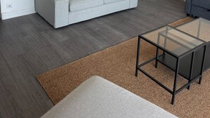Un salón moderno con un sofá gris, un cuadro de una escena marítima, una lámpara colgante de mimbre y una mesa de centro de cristal.