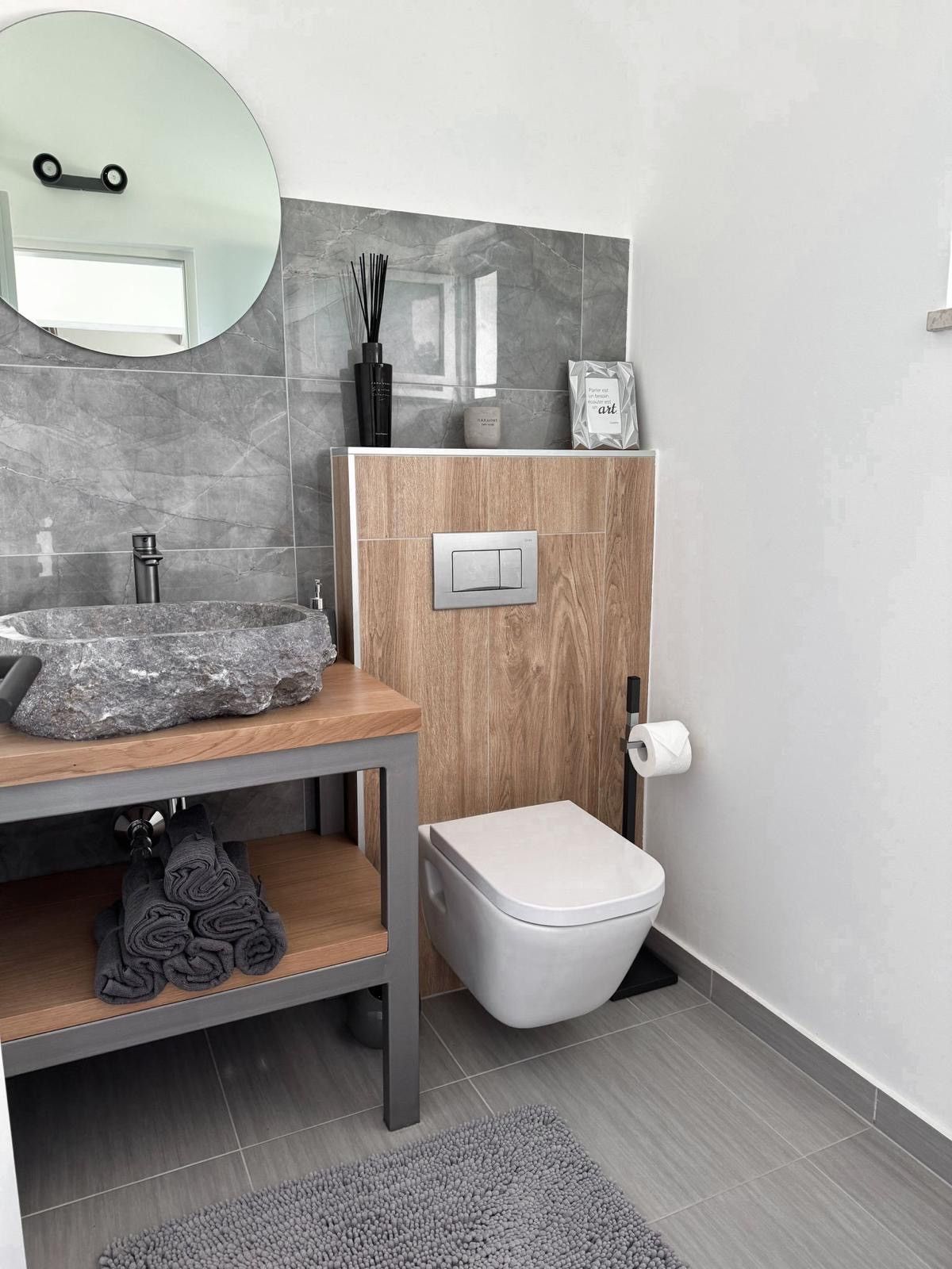 A modern bathroom with a stone sink, wooden vanity, and a toilet.