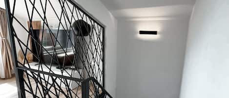 A modern staircase with a geometric metal railing, wooden steps, and a recessed light fixture.