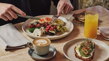 Desayuno con un plato de comida, un vaso de jugo de naranja y una taza de café sobre una mesa de madera.