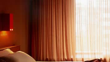 A hotel room with a bed, a nightstand, and a window with curtains.