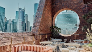 Una terraza en la azotea con un arco de ladrillo circular, muebles de mimbre blanco y un sofá a rayas.