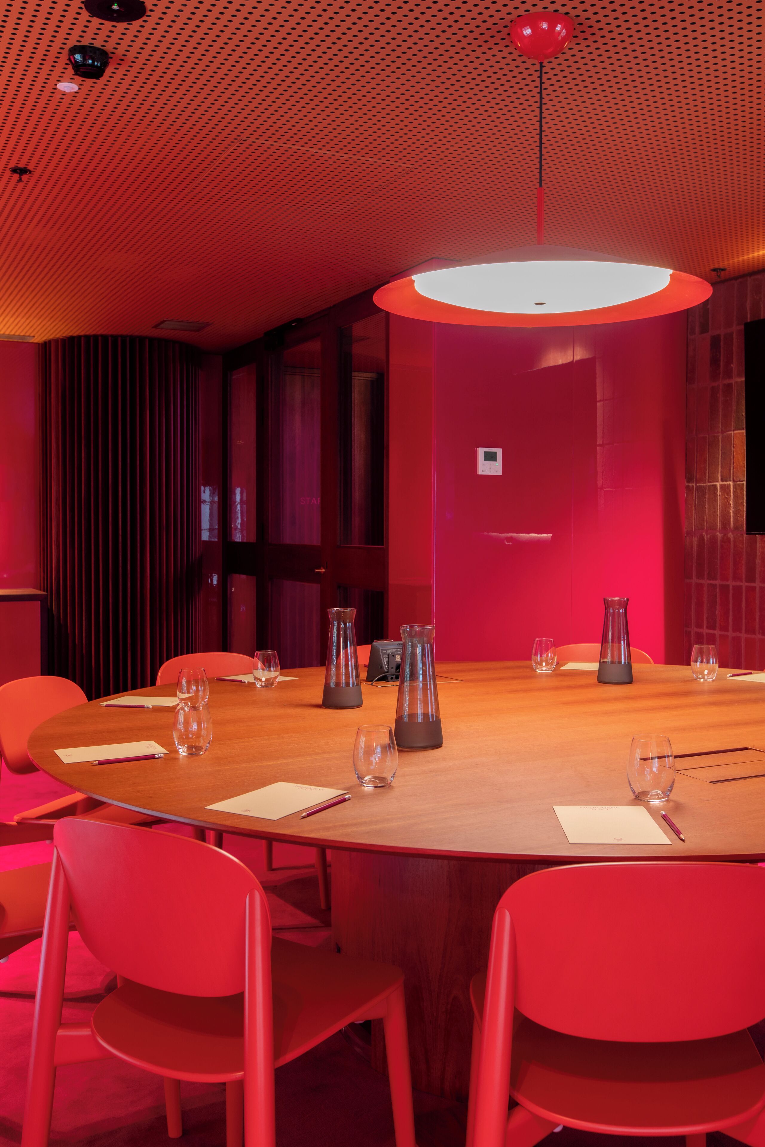 Un salón de conferencias con una mesa de madera, sillas rojas y un diseño moderno en el techo.