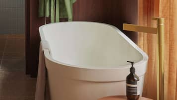 A bathroom with a freestanding bathtub, a towel rack with green towels, a bottle of shampoo, and a wooden stool.