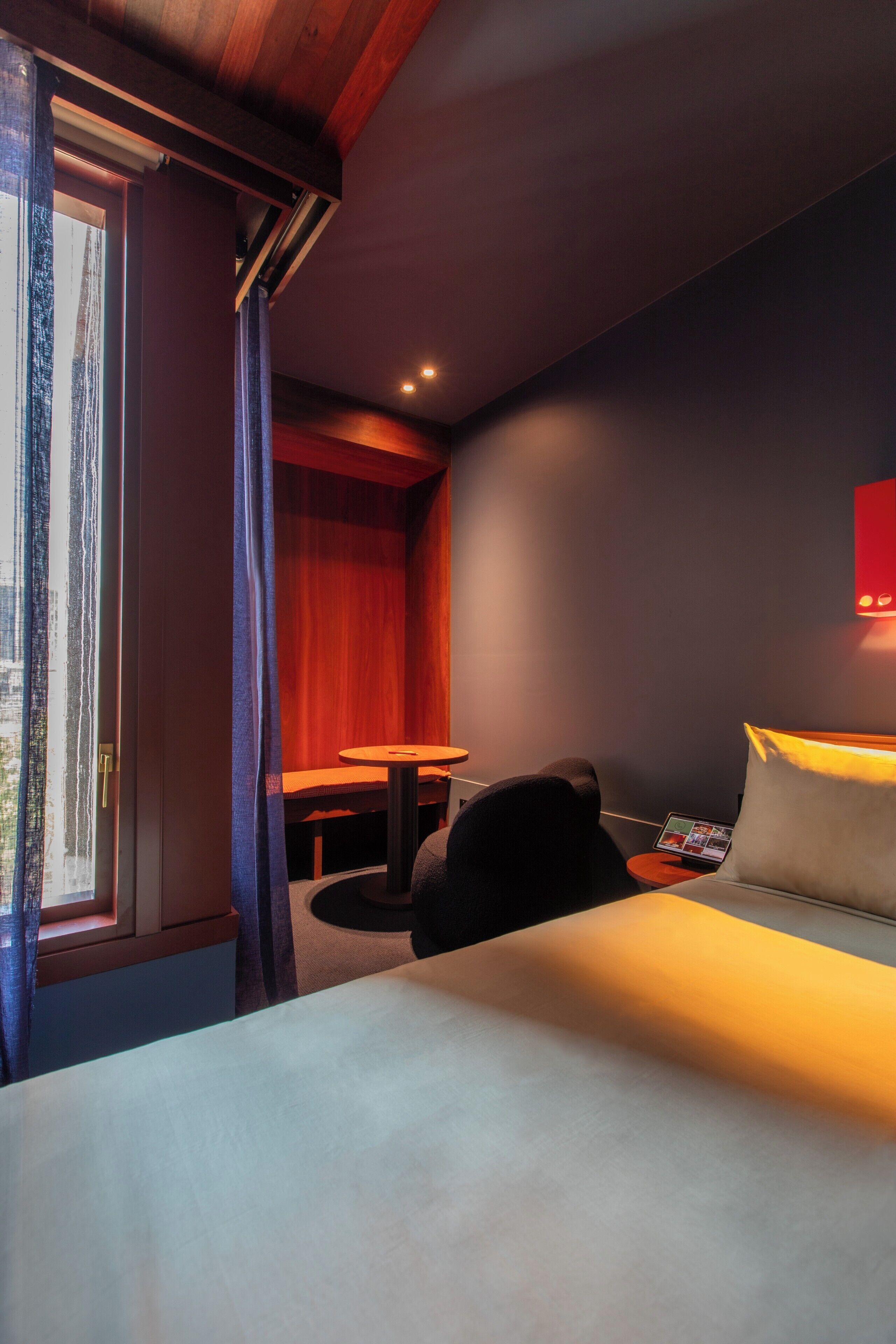 Une chambre d’hôtel avec un lit, un bureau, une chaise, une table et une fenêtre avec des rideaux.