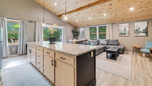 Een ruime keuken met een groot eiland, houten plafond en grote ramen met uitzicht op groen.