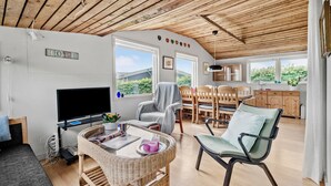 Ein gemütliches Zimmer mit Fernseher, Korbmöbeln, einem Essbereich und einer durchgehenden Tür erkennbaren Küche.