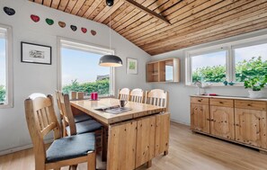 A dining area with a wooden table and chairs, a pendant light, and a view of greenery outside.