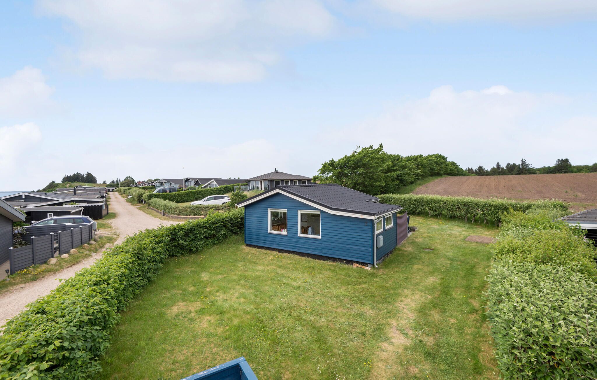 A blue mobile home with a fenced yard, surrounded by other similar homes, in a rural setting.