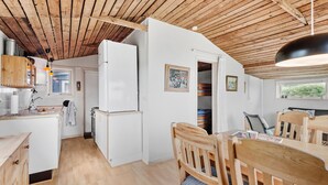 Eine kompakte Küche mit Holzschränken, einem weißen Kühlschrank und einem Essbereich mit Holztischen und -stühlen.