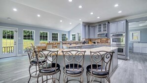 A spacious kitchen with a central island, bar stools, and modern appliances. - Poconos Home w/ Theater, Hot Tub, Sauna & Arcade (East Stroudsburg)