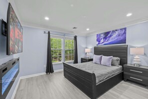Une chambre à coucher avec un lit, des tables de chevet, une télévision et une fenêtre avec des rideaux.