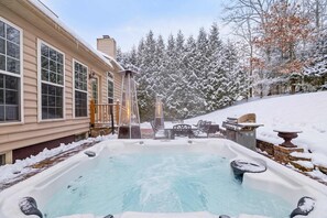A hot tub with a view of a house and snow-covered trees.