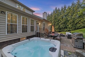 Un bain à remous, un espace salon extérieur et un barbecue, le tout aménagé dans un jardin.