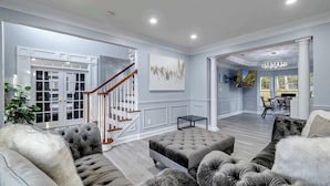 A spacious living room with a grand staircase, plush seating, and a view to the dining area.