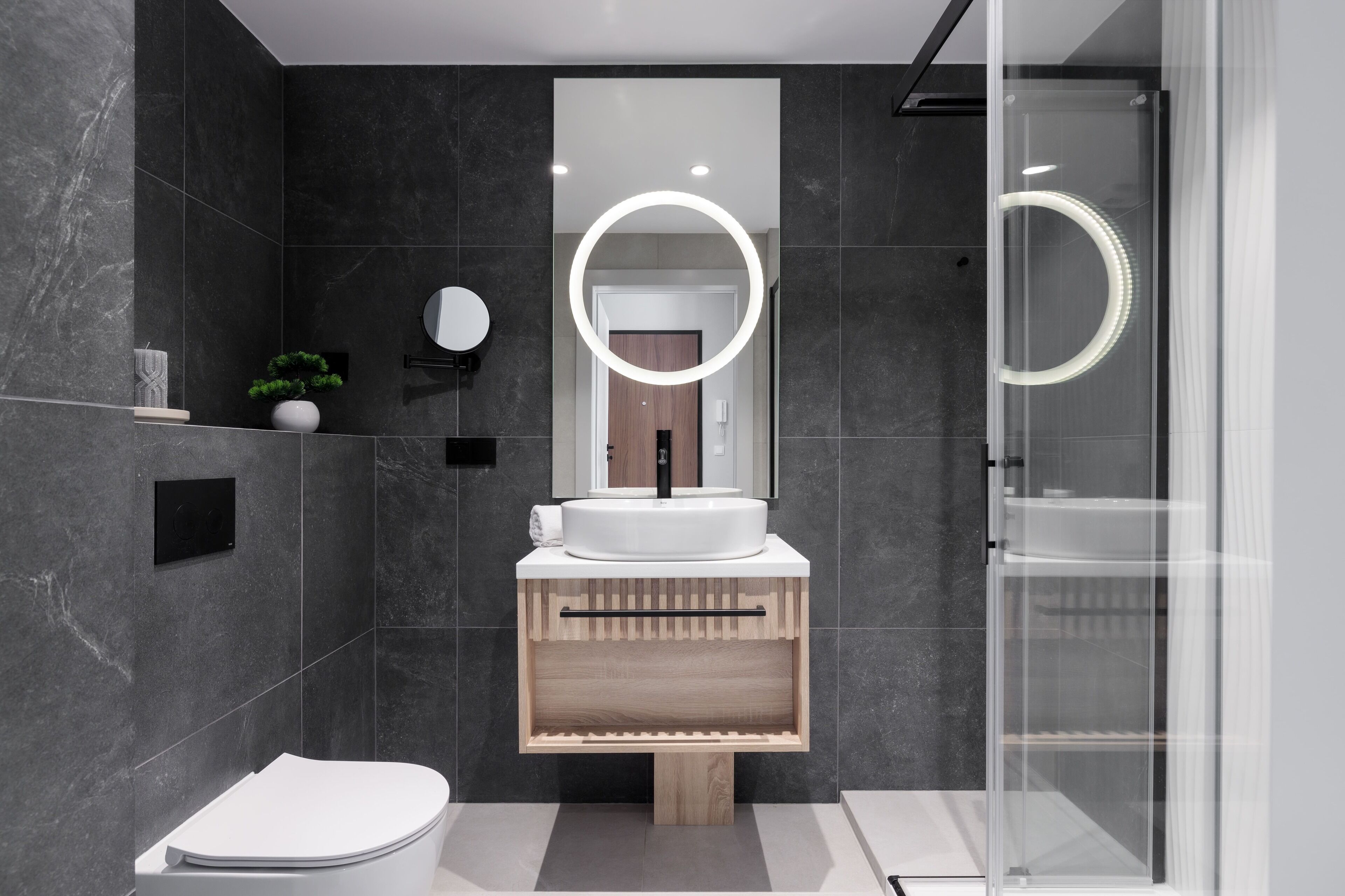 A modern bathroom with a white sink, a mirror with a circular light, and a shower enclosure.