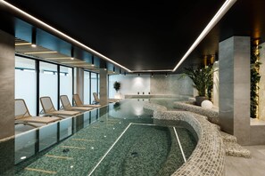 A modern indoor pool with a glass barrier, lounge chairs, and a mosaic-tiled edge. - Baltic Waves Resort by PI Apartments (Miedzyzdroje)