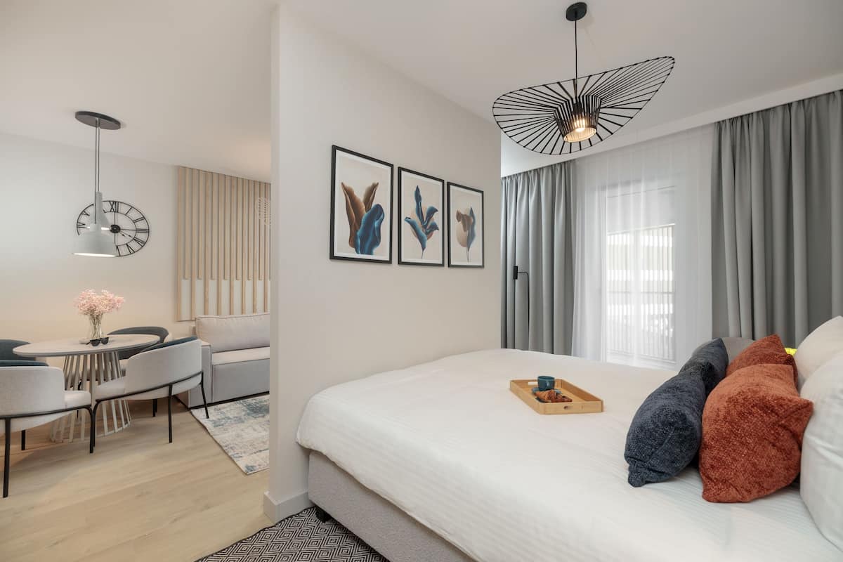 Une chambre d’hôtel moderne avec un grand lit, un bureau avec une chaise, une horloge au mur et un luminaire au plafond au design original.