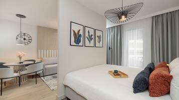 A modern hotel room with a large bed, a desk with a chair, a clock on the wall, and a unique ceiling light fixture.