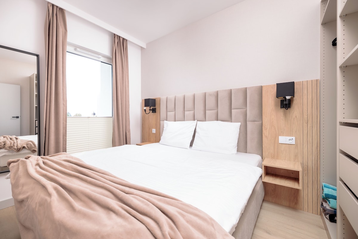 A modern hotel room with a large bed, a bedside table, a wardrobe, and a window with curtains.