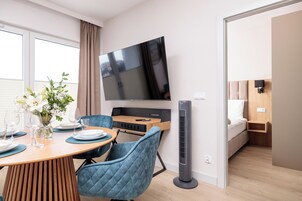 Una habitación moderna con una mesa de comedor, sillas, un televisor montado en la pared, una cama y un calefactor portátil.