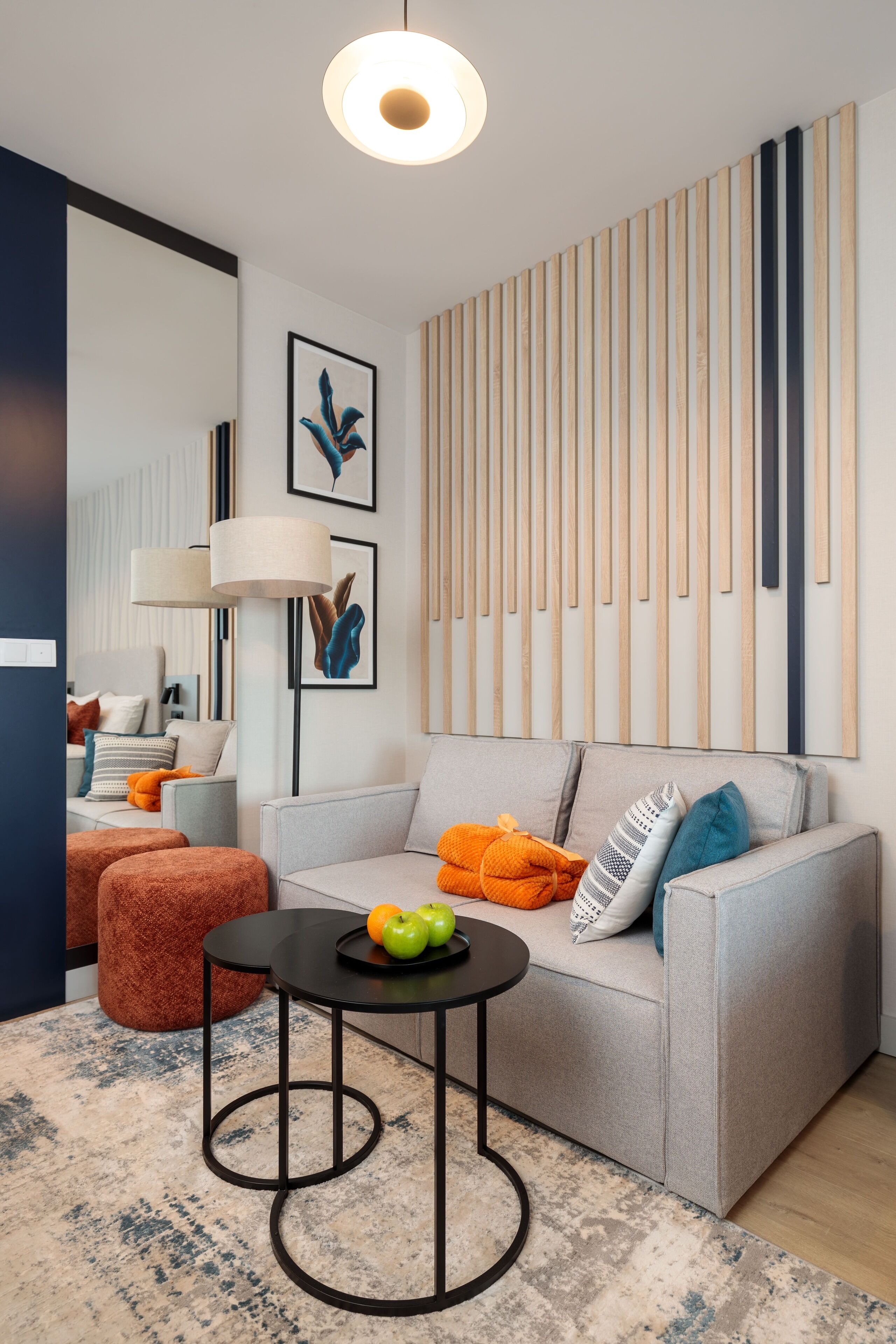 A modern living room with a grey sofa, a round coffee table, and a wooden slat wall panel.
