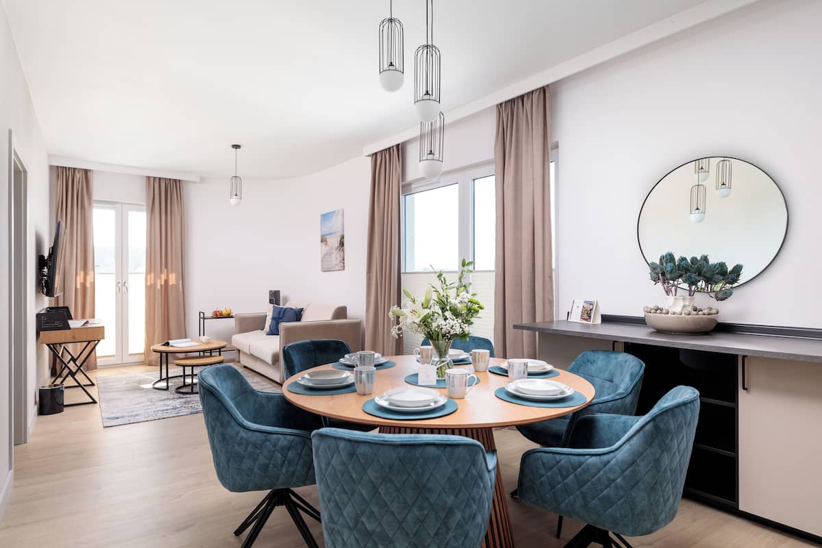 Un espace repas moderne avec une table ronde pour six personnes, des chaises rembourrées en tissu bleu et un grand miroir au-dessus de la table.