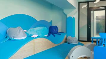 Zona de juegos infantiles con diseño inspirado en las olas, que incluye un banco con forma de ola y un cojín con forma de tiburón.