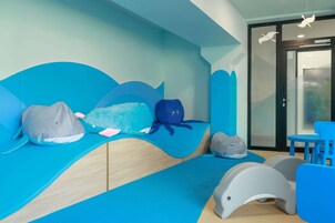 Zona de juegos infantiles con diseño inspirado en las olas, que incluye un banco con forma de ola y un cojín con forma de tiburón.