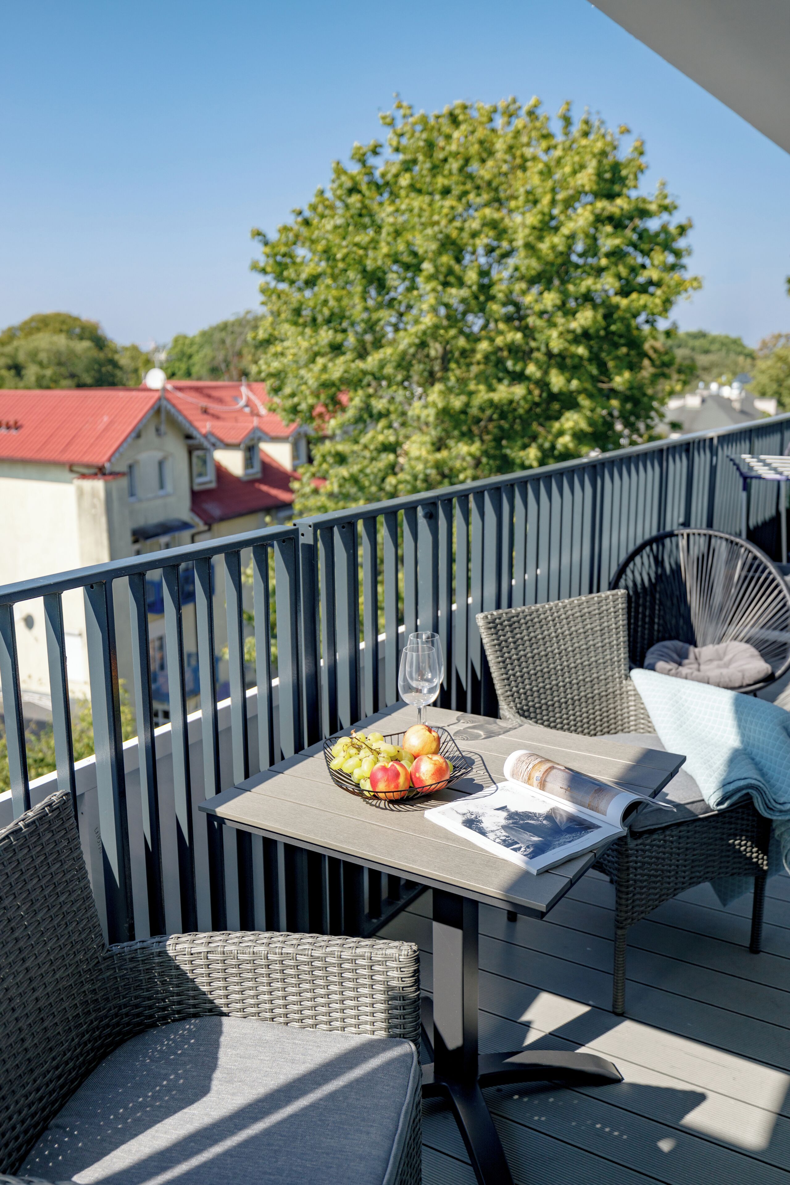 Un balcon agrémenté de meubles en osier, une table avec un verre et un saladier rempli de fruits.