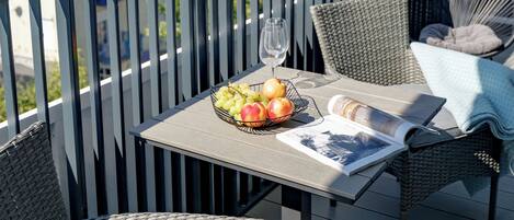 Ein Balkon mit Korbmöbeln, einem Tisch mit einem Glas und einer Schale Obst.