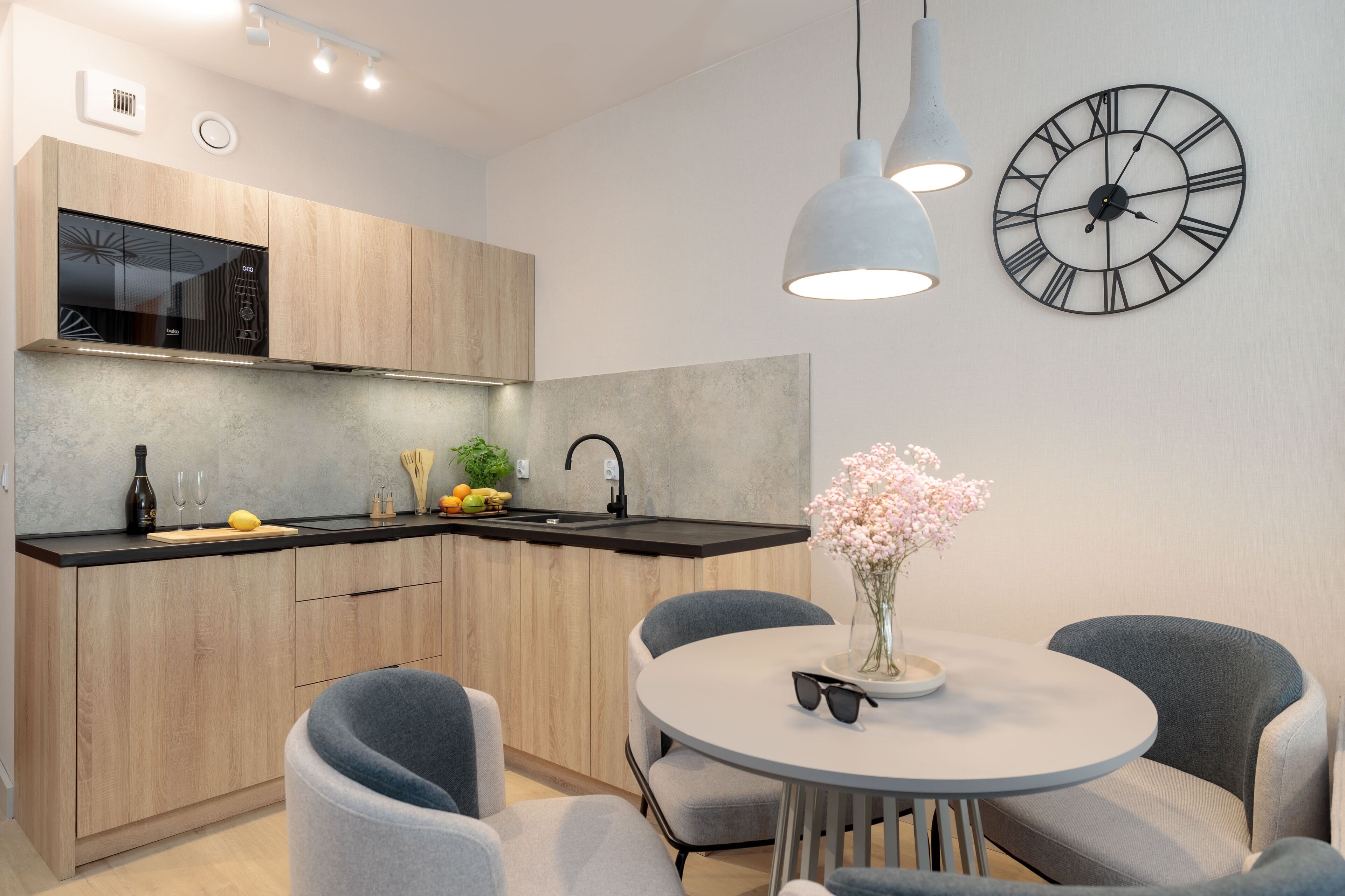 Una cocina moderna con armarios de madera, un microondas negro y un lavamanos. Hay una mesa redonda con sillas y un florero con flores.