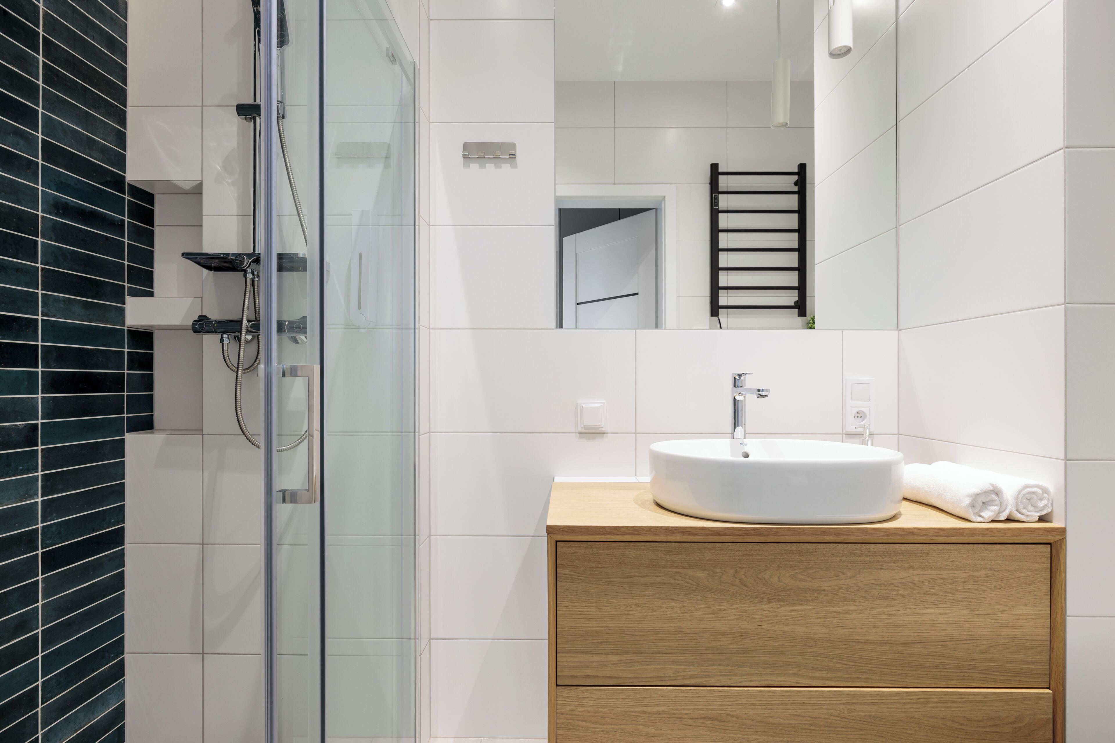 A modern bathroom with a glass-enclosed shower, a white sink, and a wooden vanity.