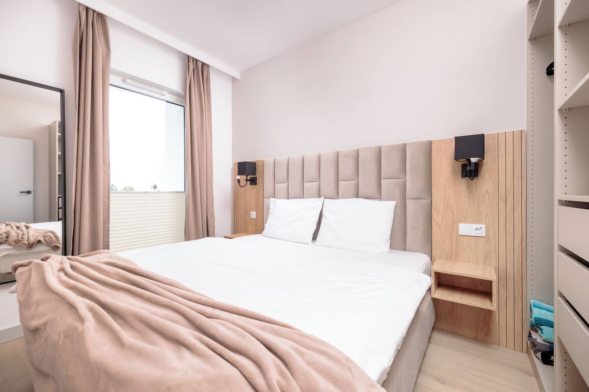 Une chambre d’hôtel bien aménagée, avec un grand lit, une table de chevet, une armoire et une fenêtre avec des rideaux.