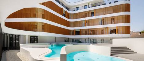 Un edificio moderno de varios pisos con una piscina central, terrazas al aire libre y fachadas de madera y vidrio.
