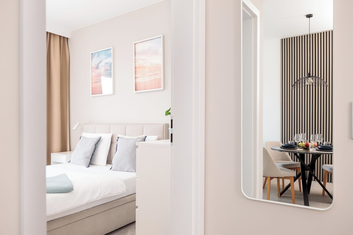 Une chambre d’hôtel moderne, équipée d’un lit, d’un coin repas avec une table et des chaises, et d’un miroir qui reflète la pièce.