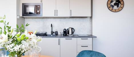 A modern kitchen with white cabinets, a microwave, and a kettle. There is a dining table with plates and glasses, and a vase of flowers.