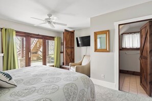 Een slaapkamer met een bed, een stoel, een televisie en een houten deur.
