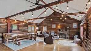 A log cabin interior with a dining area, seating, and a fireplace.