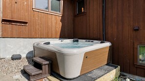 Een hottub voor een houten gebouw met ramen en een klein opstapje.